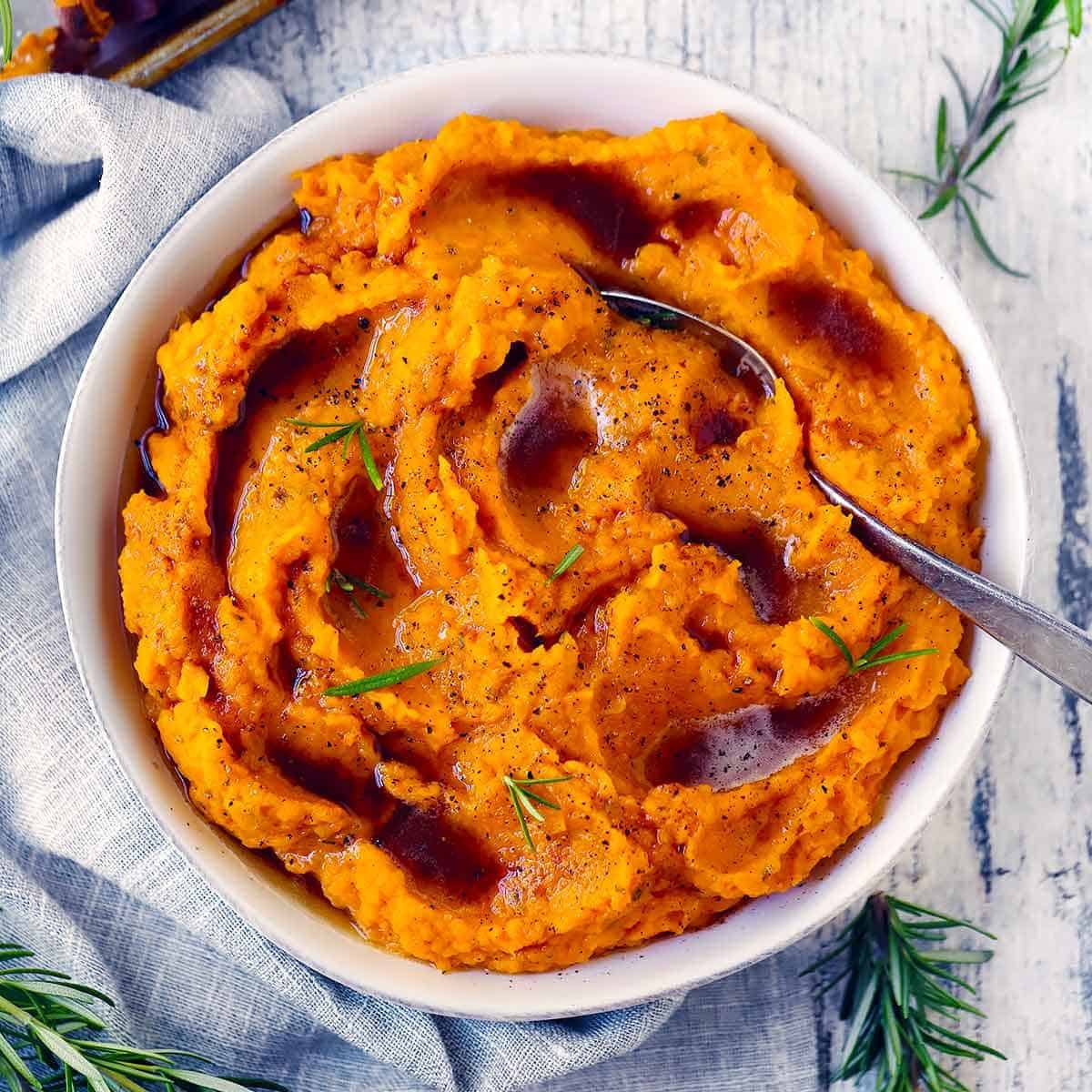 Square photo of a bowl of mashed butternut squash and sweet potato with brown butter, rosemary, and maple.