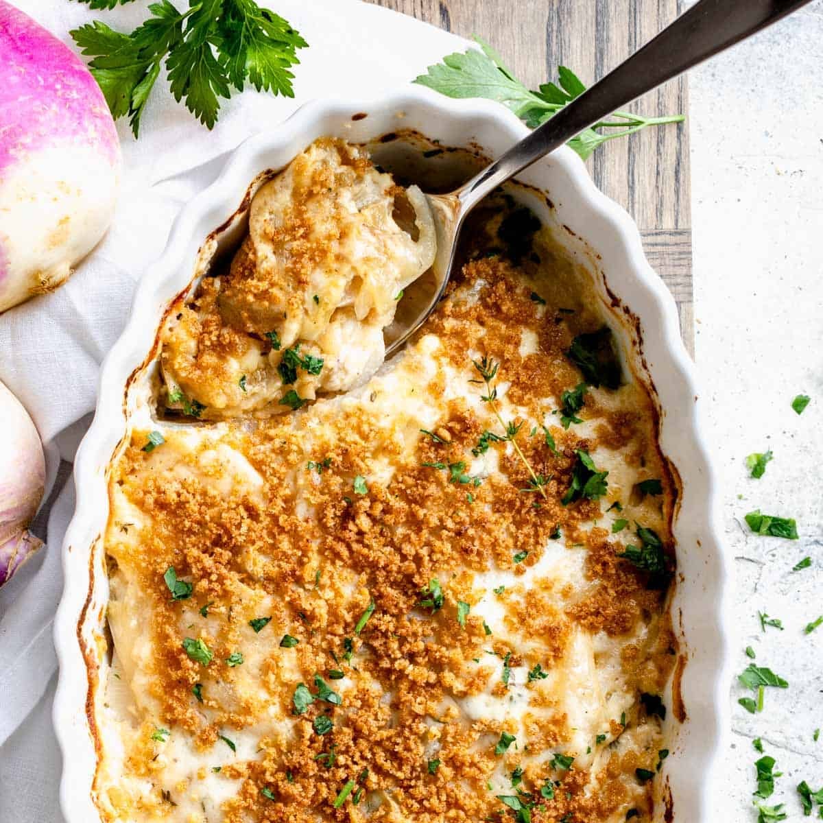 turnip casserole in scalloped white baking dish with serving spoon