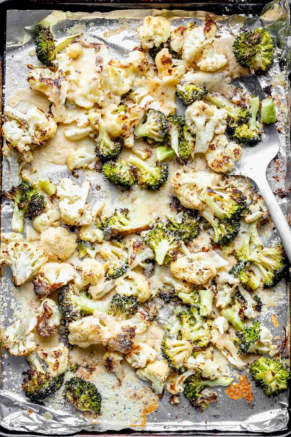 A close up of a sheet pan with roasted broccoli and cauliflower with cheese melted on it.