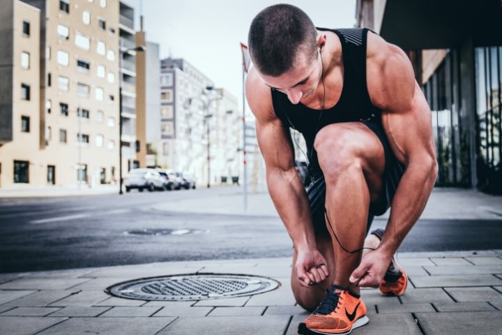 muscular guy in black tank top tieing shoe lace of orange shoes