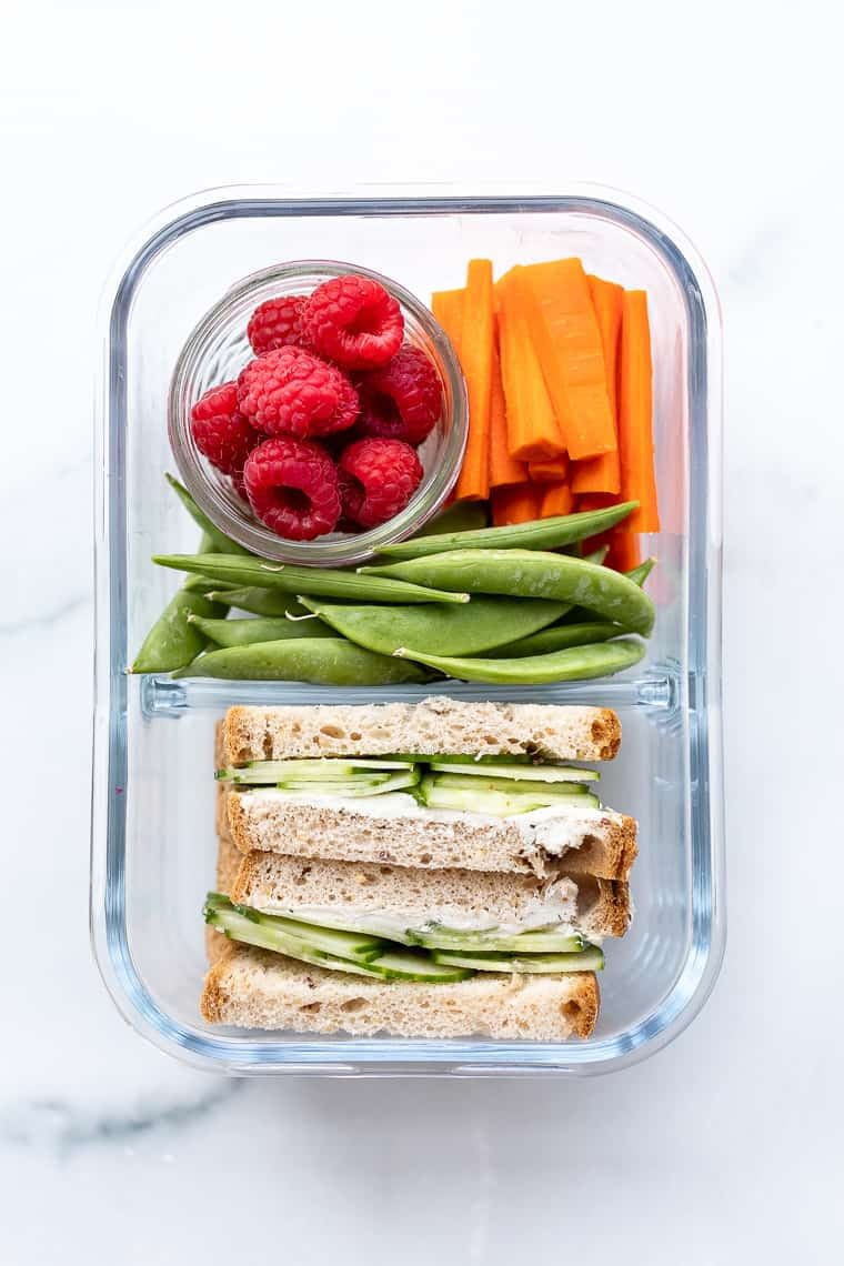 overhead of a glass bento box with fresh berries, vegetables and a sandwich