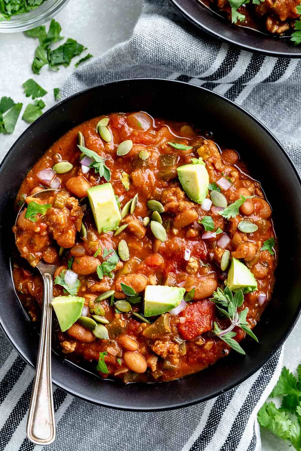 turkey chili in a black bowl from overhead with garnishes and avocado on top