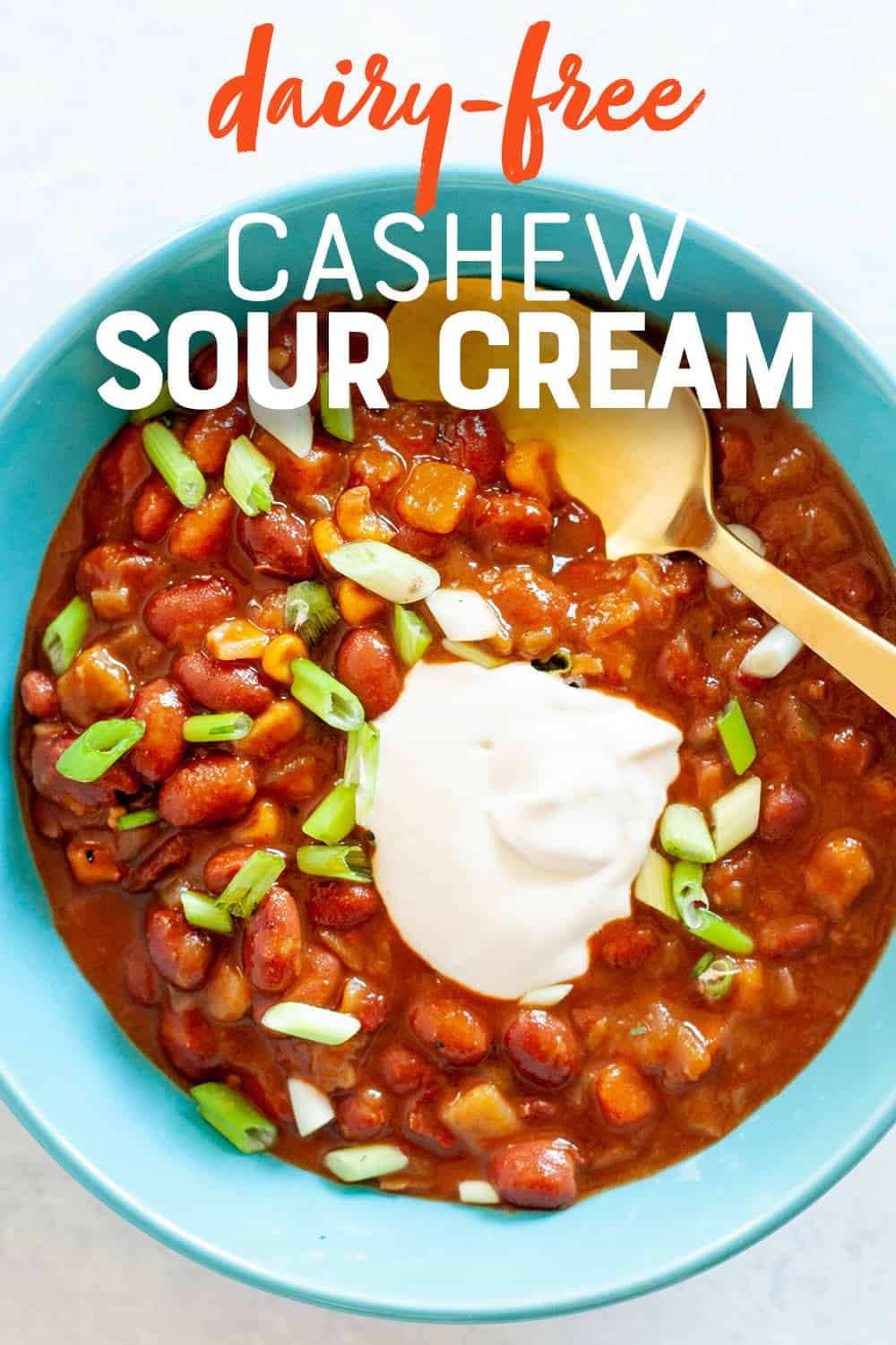 Cashew sour cream on top of chili in a blue bowl. A text overlay reads, "Dairy-Free Cashew Sour Cream."