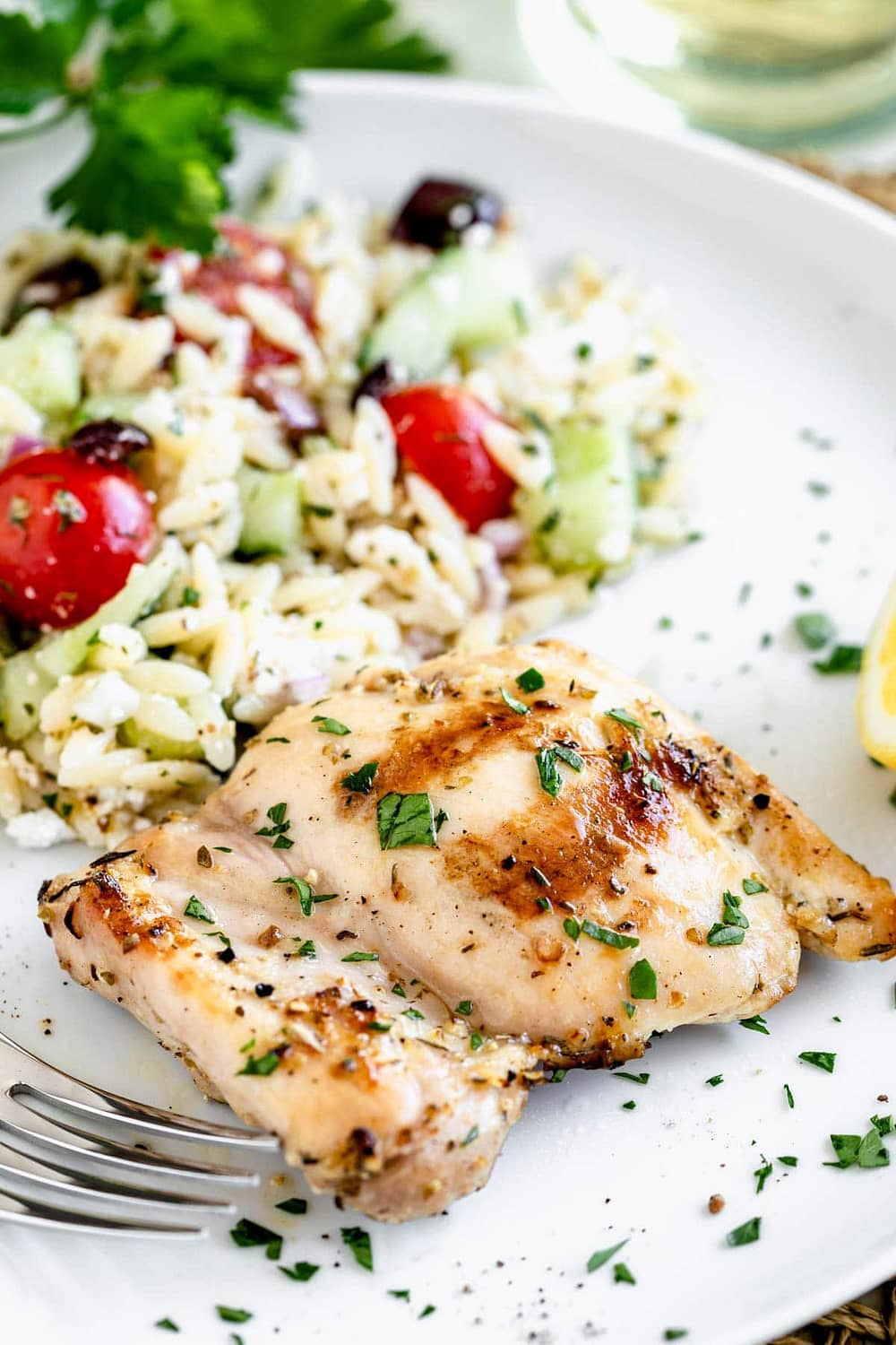 a grilled chicken thigh on a plate with orzo salad