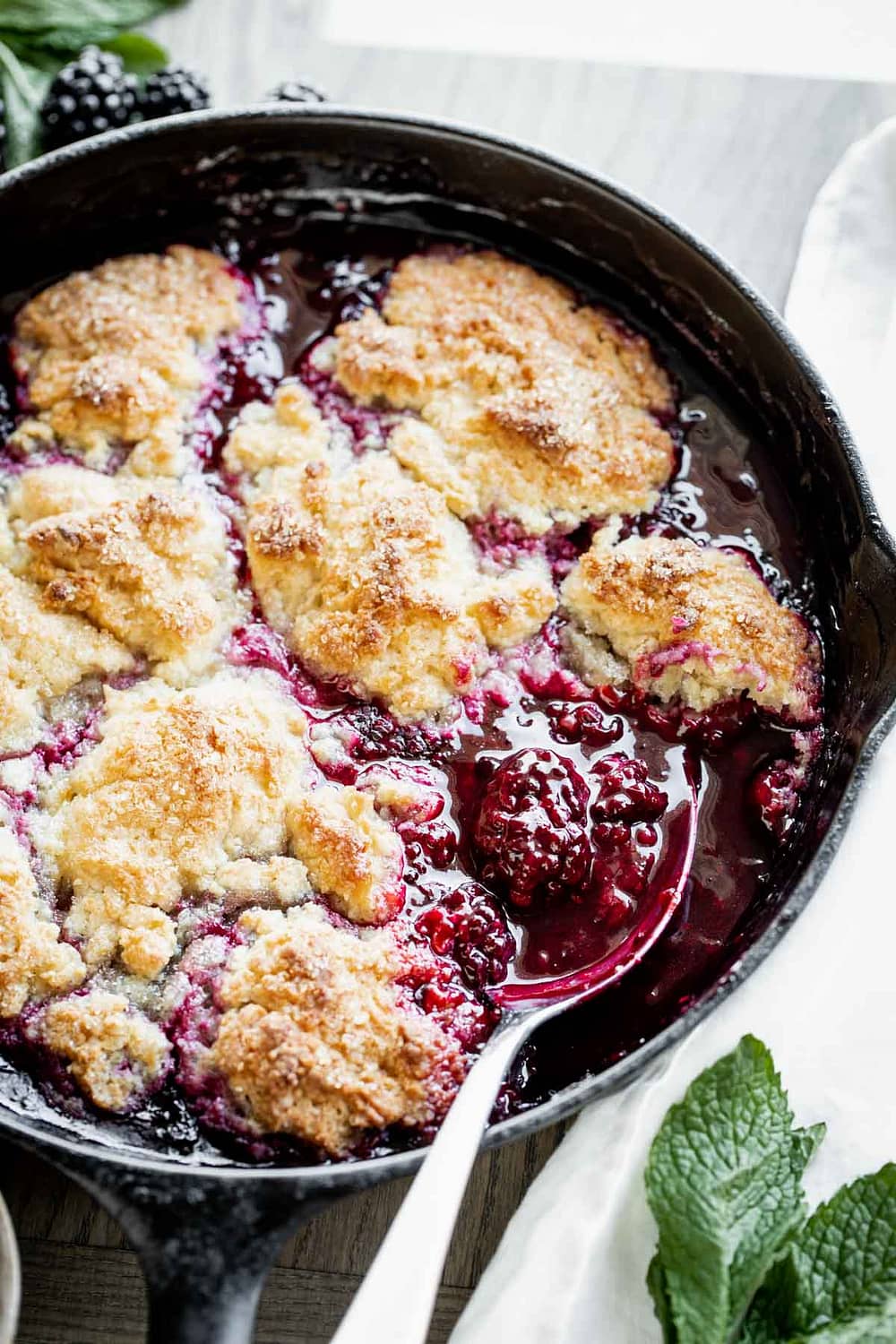 Blackberry cobbler in a skillet with a spoon in it.