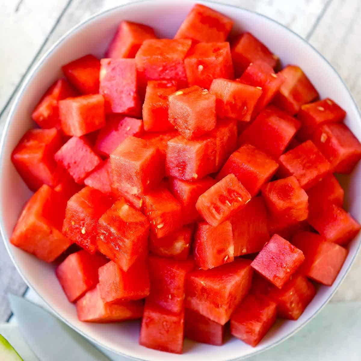 Square photo of cubed watermelon in a white bowl.