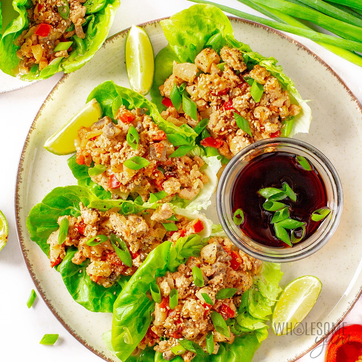 Healthy Asian chicken lettuce wraps on a plate with garnishes.