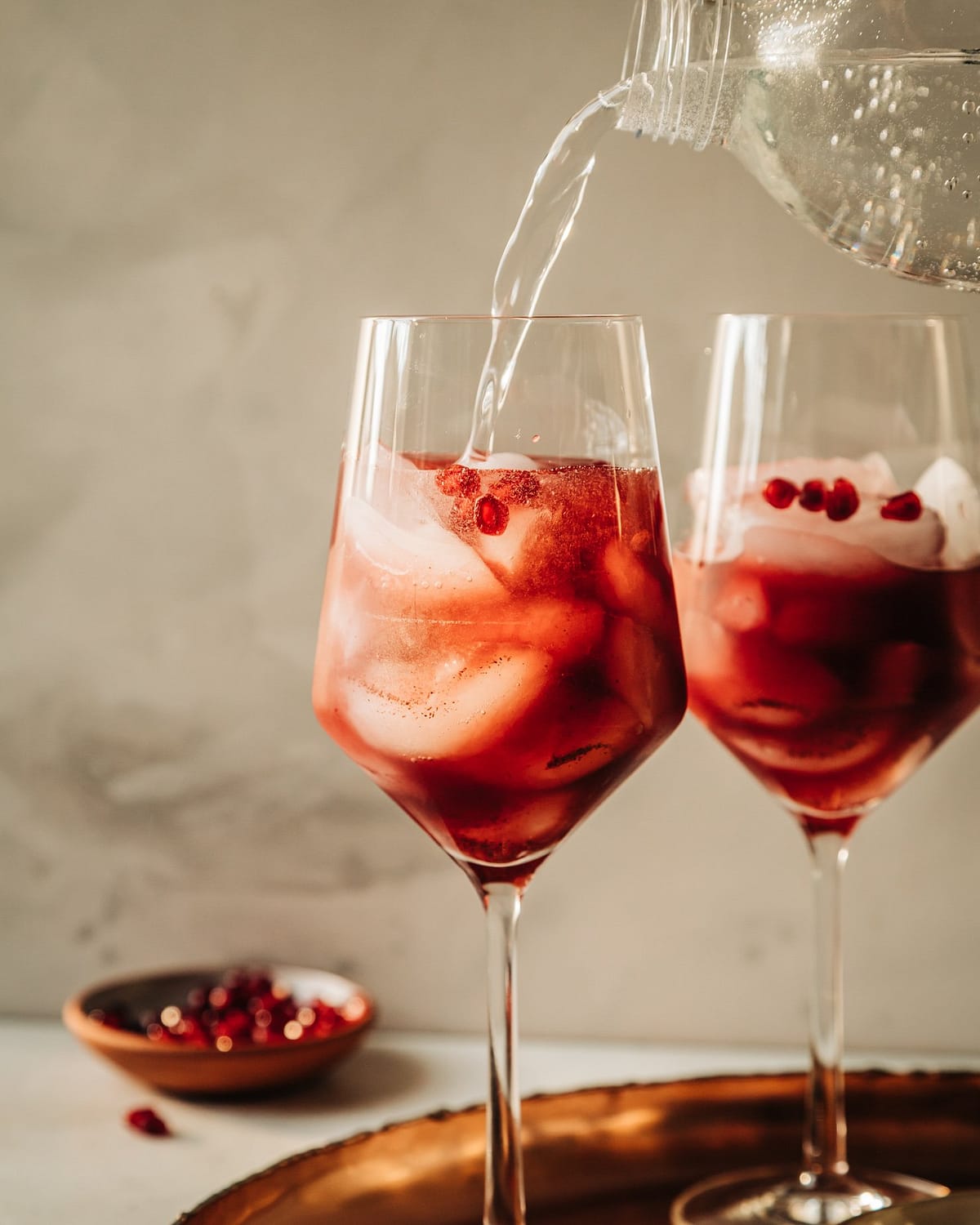 A head-on shot shows sparkling water topping off a pomegranate pomander spritz mocktail in a wine glass.
