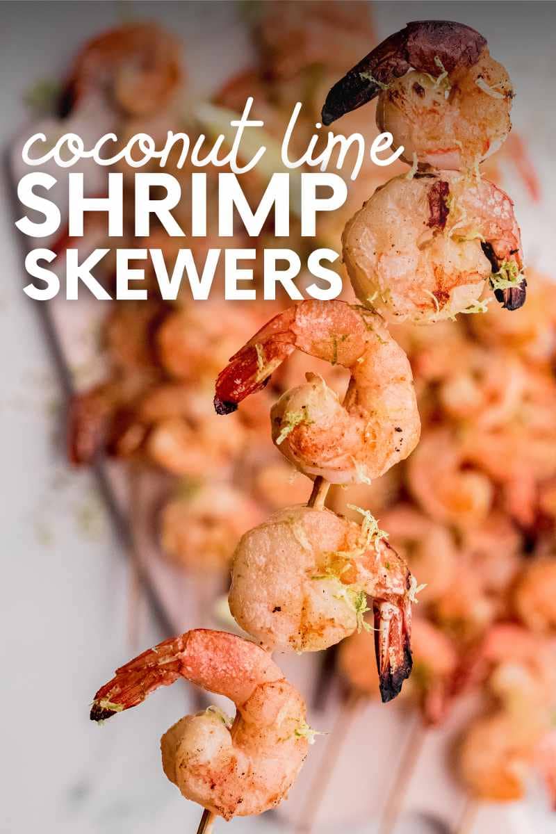 Tight view of a shrimp skewer garnished with lime zest held up above a platter of additional kabobs. A text overlay reads, "Coconut Lime Shrimp Skewers."